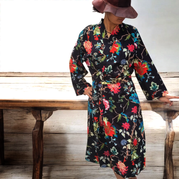 This striking cotton kimono robe features a bold and colorful botanical and avian print against a dark background. The robe showcases a vivid combination of flowers, leaves, and birds in shades of green, blue, red, and yellow. It has a relaxed, open-front design, with a matching belt to cinch at the waist for an adjustable fit. The fabric is soft, breathable cotton, making it comfortable for casual lounging or as a statement piece. The unique print and lightweight material make it perfect for adding a pop of color to your wardrobe